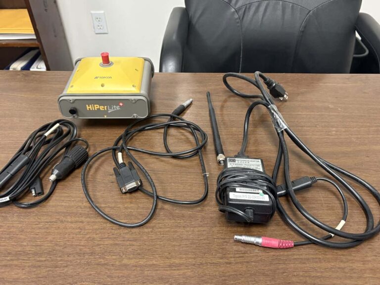 Topcon HiPer Lite GNSS receiver with cables and accessories on desk.