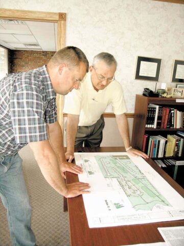 Two land surveyors examining detailed site plans on a table.