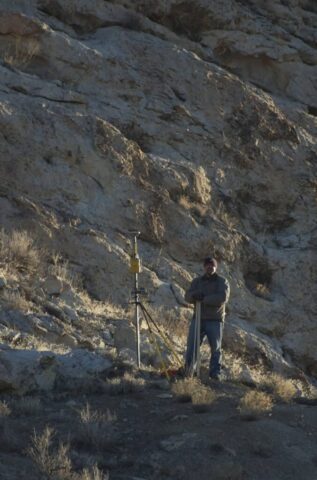 Surveyor operating total station on rocky terrain for land measurement.