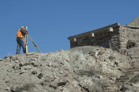 Land surveyor with theodolite on rocky terrain at a construction site.