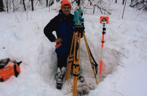 Surveyor using equipment in snow for land measurement and mapping.