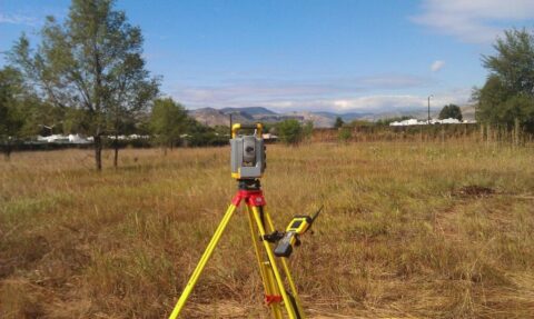 Total station surveying instrument on tripod in open field.