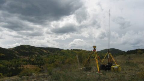 Land survey equipment set up in a rural landscape under cloudy sky.