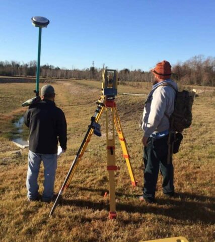 Two surveyors using a total station for land measurement in open field.