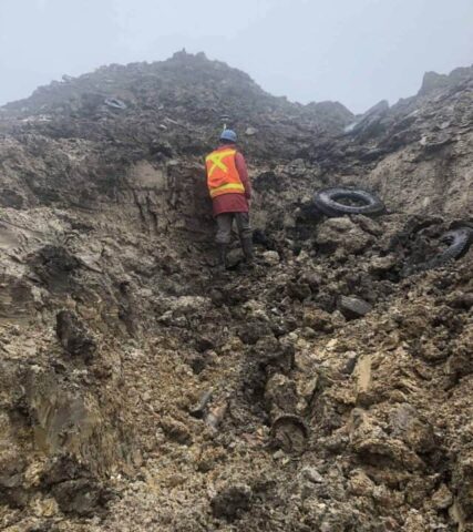 Surveyor in safety gear examining rocky slope for land assessment.