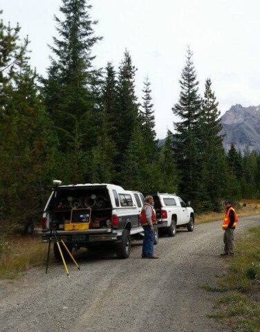 Surveyors working in a forested outdoor environment with equipment.