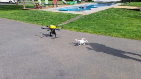 Two drones on pavement near pool and grassy area.