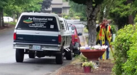 Surveyor with equipment near survey vehicle on residential street.