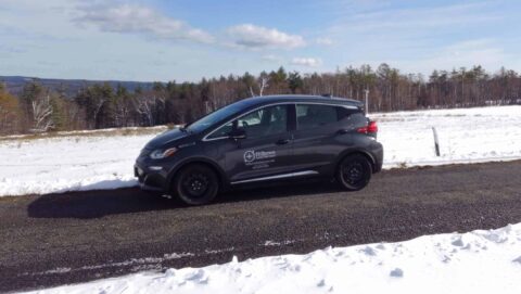 Black surveyor vehicle parked on rural road with snow and trees in background.