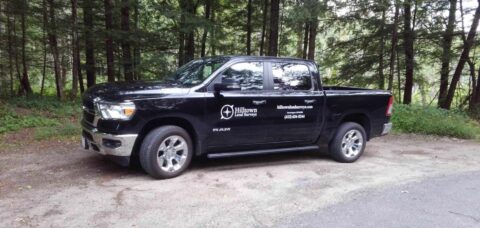 Black pickup truck with survey company logo parked in wooded area.