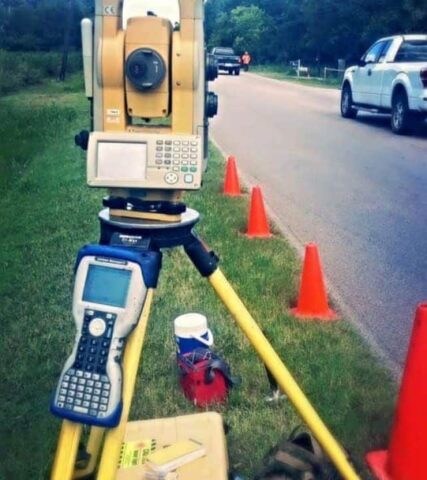 Surveying instrument with cones on roadside for land measurement.
