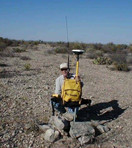 Surveyor using GPS device in arid landscape for land measurement.
