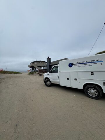 Surveying vehicle on beach with residential building in background.